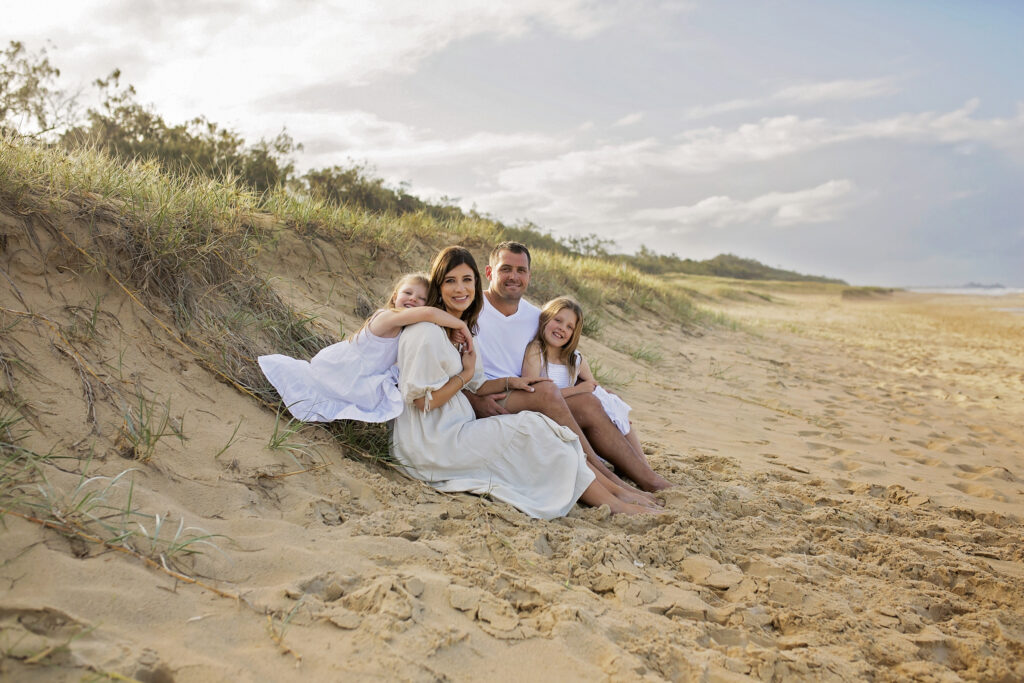 family of four sitting on the beach smiling