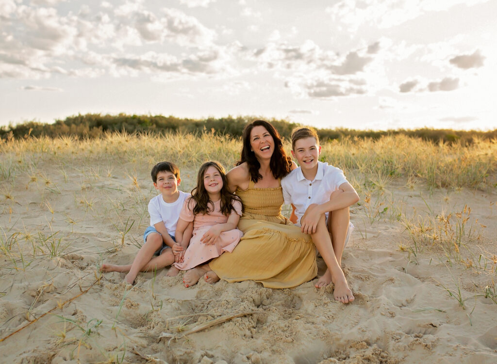 mother with her 3 kids smiling sitting on the beach