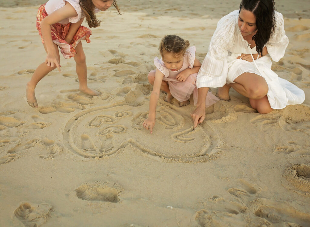 two girls and mum drawing a love heart in the sand