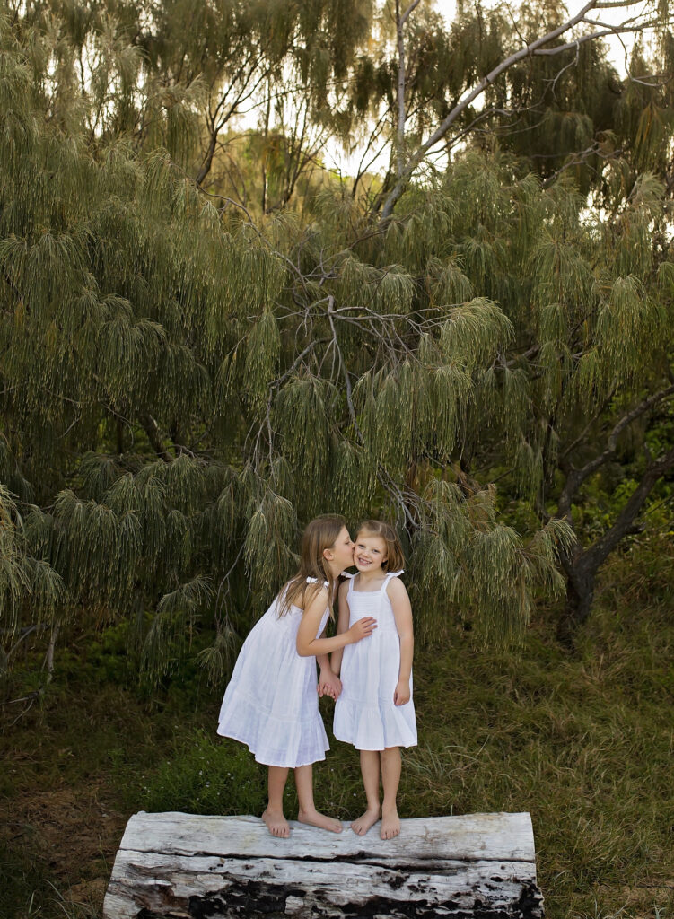 two sisters standing on a log sharing a kiss