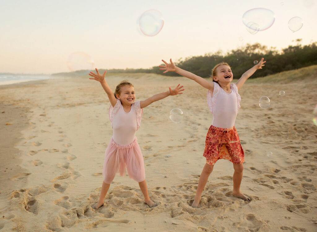 two girls on the beach laughing with bubbles floating by
