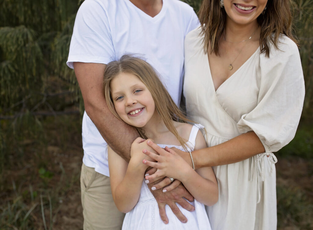 girl smiling wrapped in mum and dad's arms