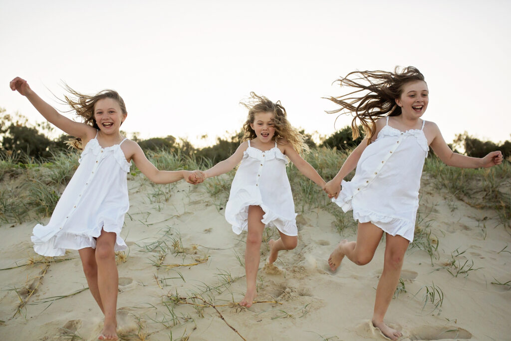 3 girls running down a sand dune on the beach
