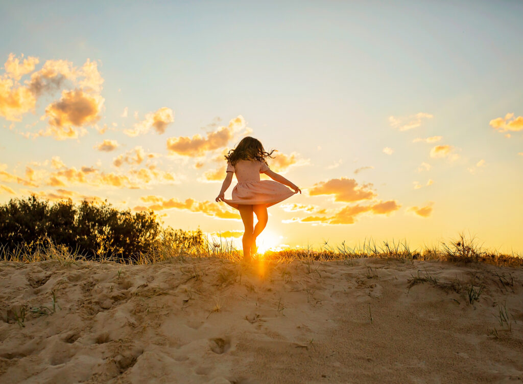girl dancing on top of a sand dune with the sunset behind her