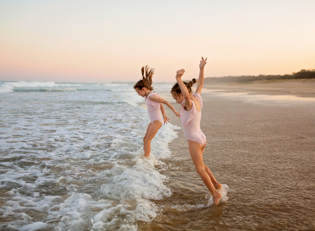 two girls jumping in the waves on the beach, two sisters on the beach