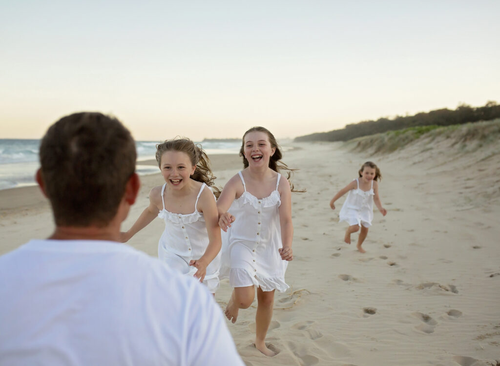 3 girls running towards their dad on the beach