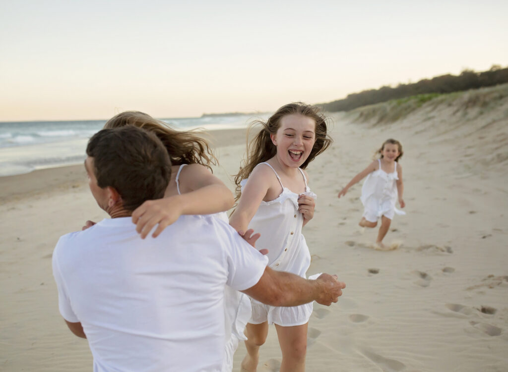 3 girls running towards their dad on the beach