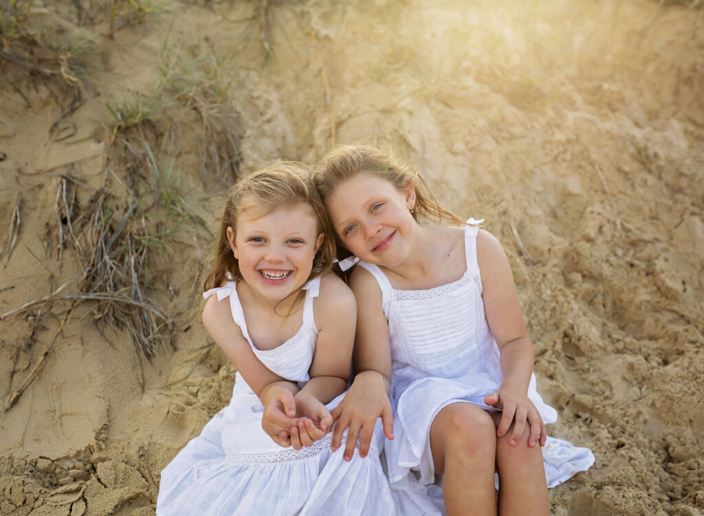 2 sisters sitting on the beach smiling