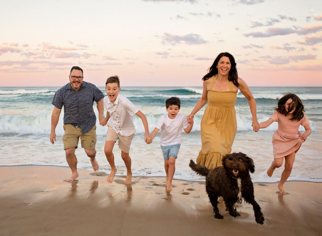 family of 5 with their dog running from the ocean behind them