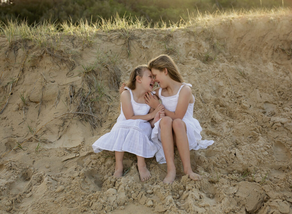 two sisters sitting on the beach touching noses