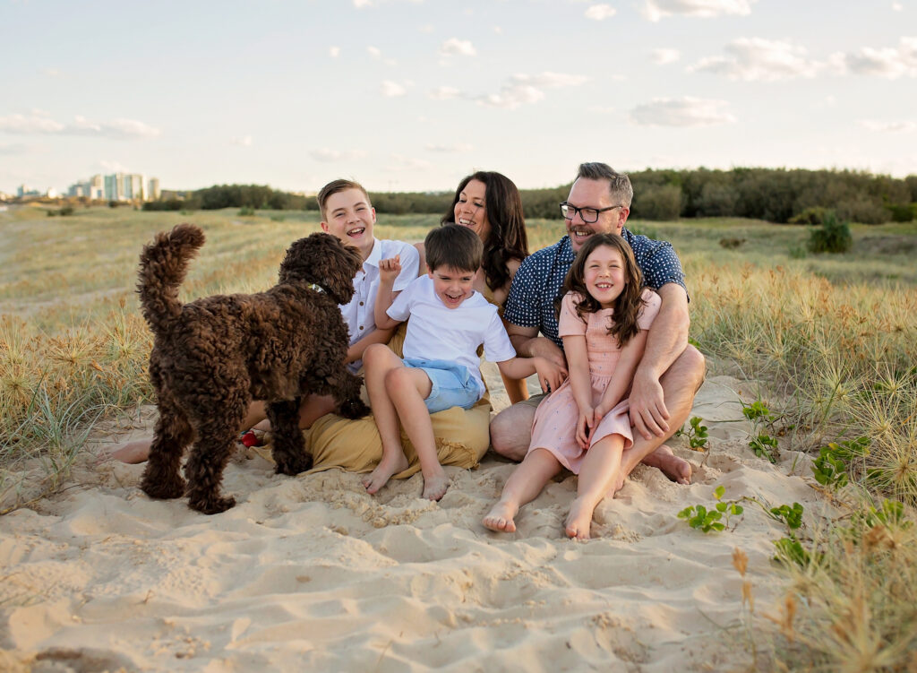 family sitting on the beach with their brown dog, smiling happy family on the beach