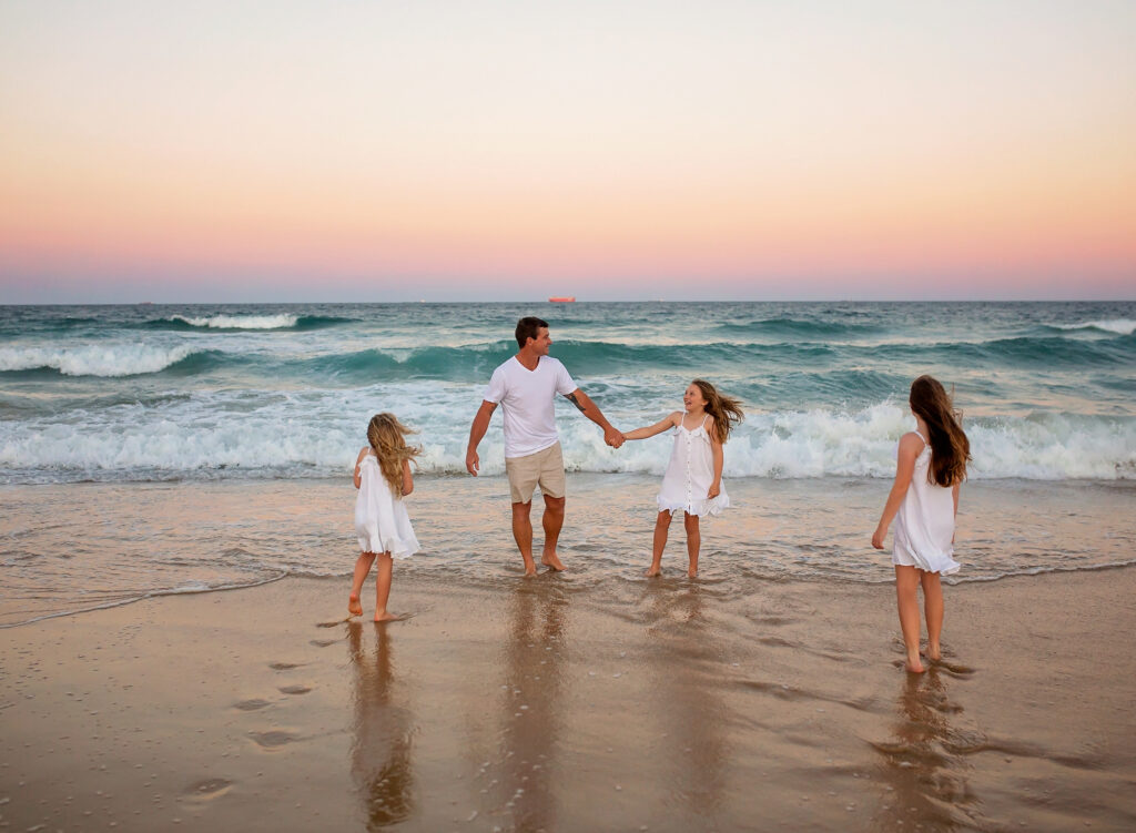 Dad playing with his 3 daughters on the beach in the waves