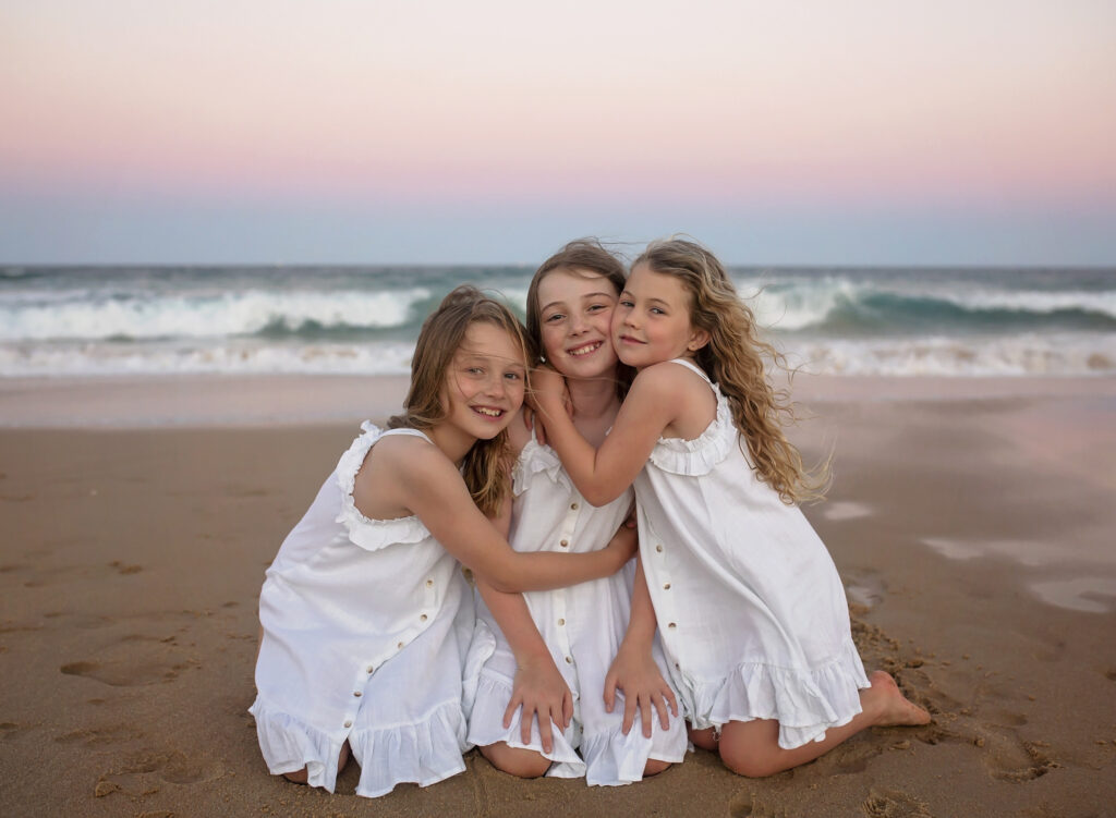 3 sisters hugging sitting down on the beach