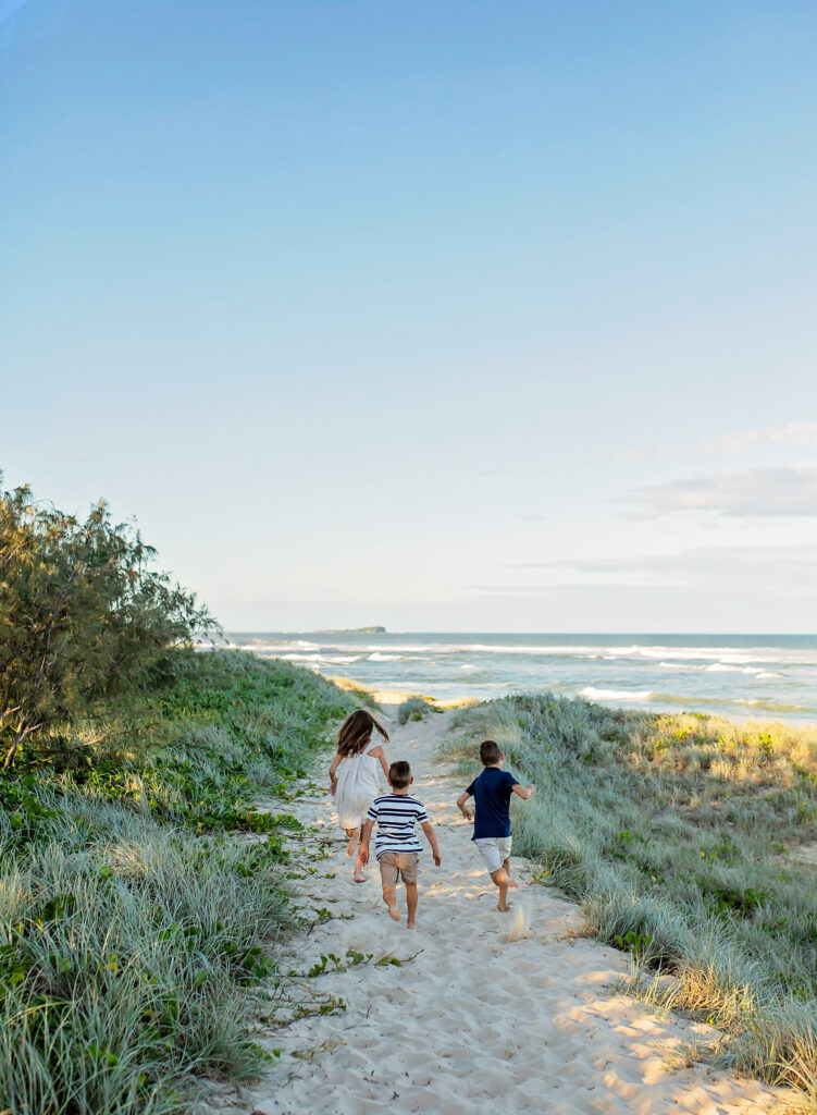 three sibling running down a sandy path on top of a sand dune