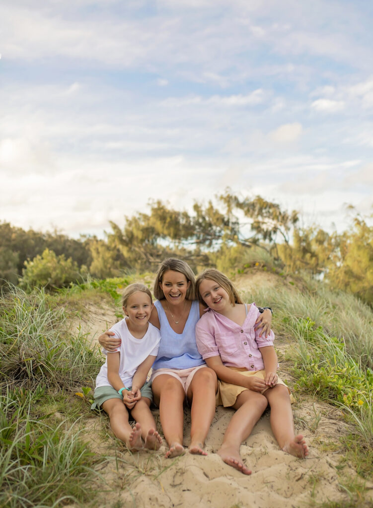 mother and two daughters sitting on a sand dune on the beach
