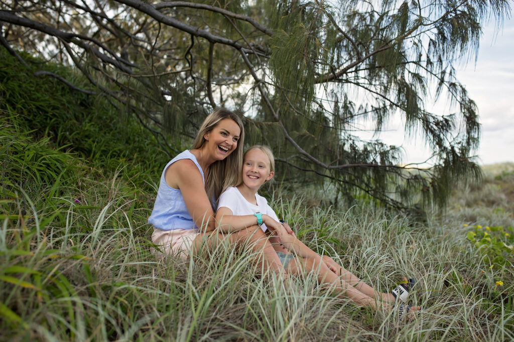 mother and daughter sitting on  a sand dune smiling