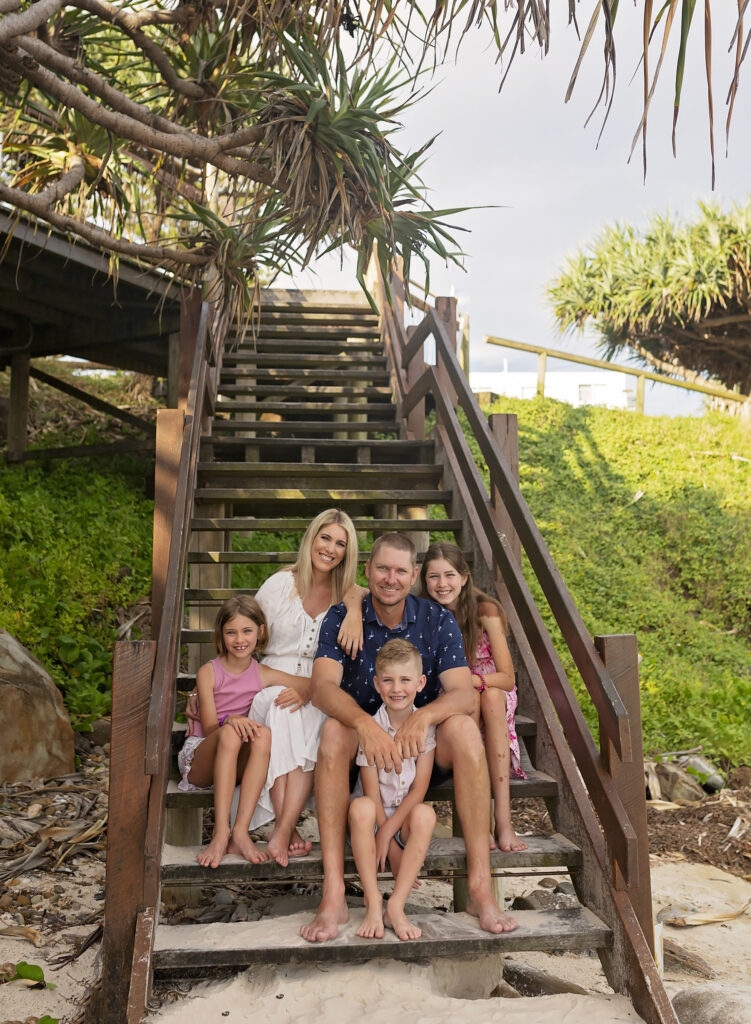 a family of 5 sit on steps at the beach