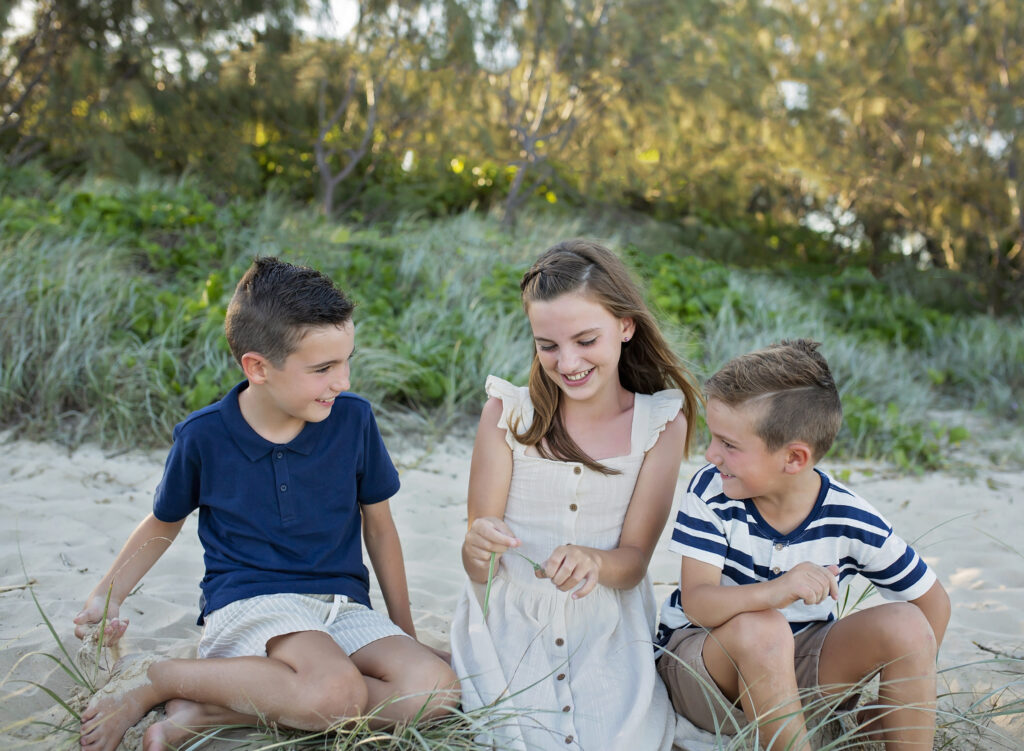 three siblings sitting on a sand dune talking