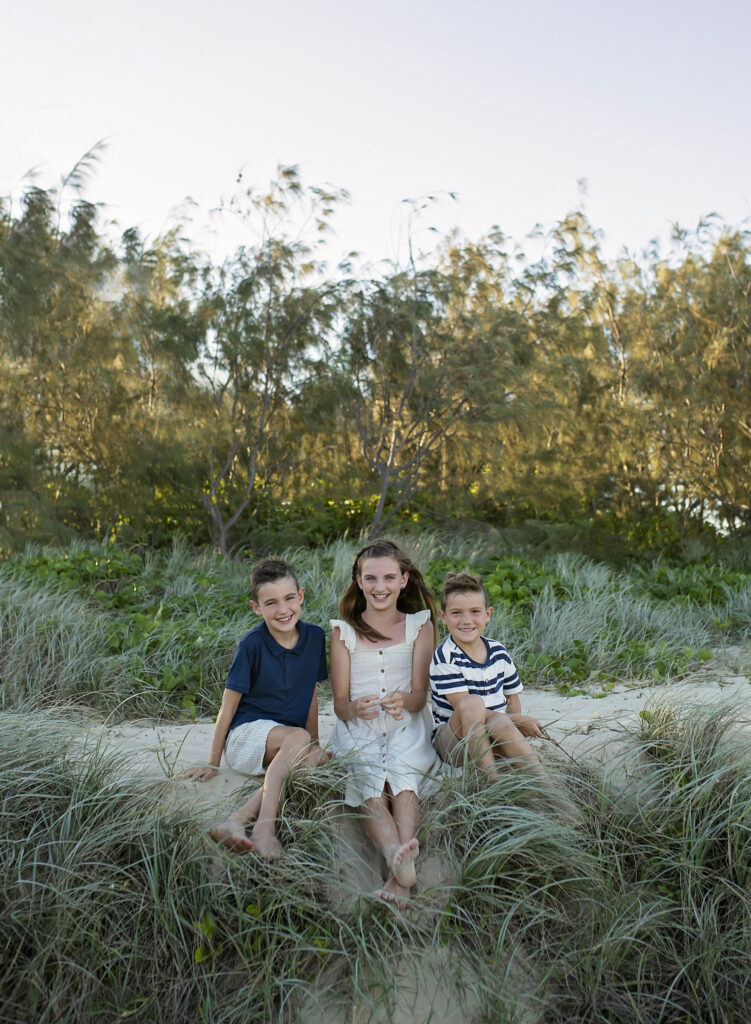three siblings sitting on a grassy sand dune on the beach