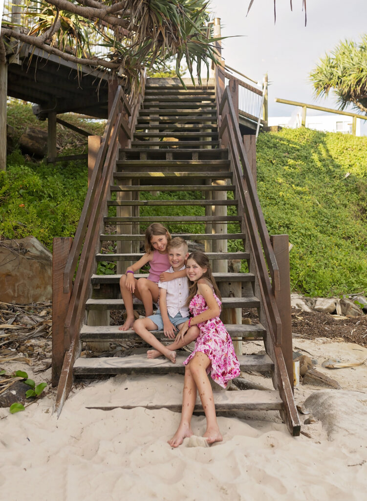 2 sisters and a brother sit on steps at the beach