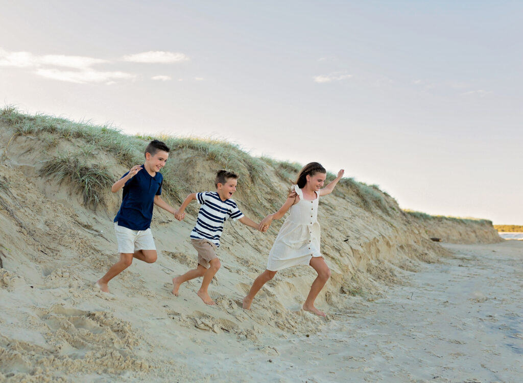 three siblings running down sand dunes on the beach