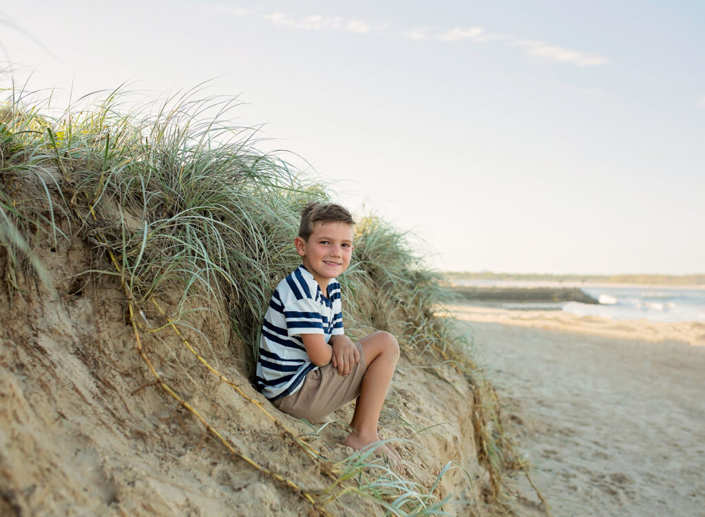 young boy sitting on the sand dune on the beach