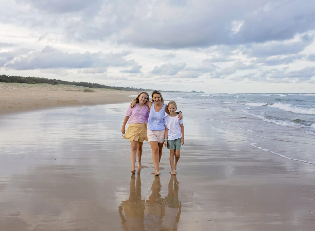 mother and two daughters walking along the beach holding each other