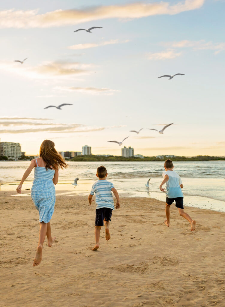 three kids running towards seagulls on the beach