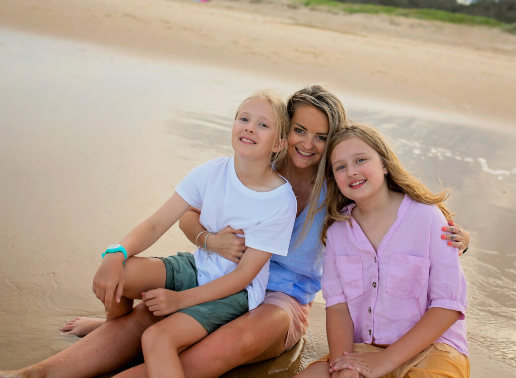 mother and two daughters sitting on the beach smiling