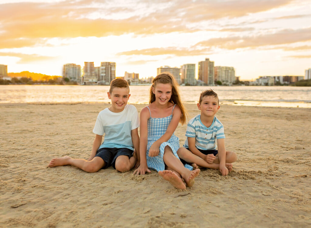 3 siblings sitting on a sand at the beach