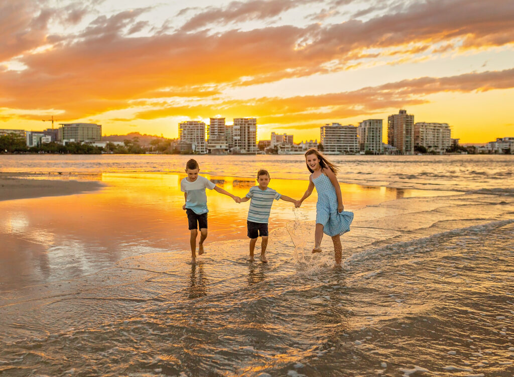 three kids playing in the shallow water at sunset