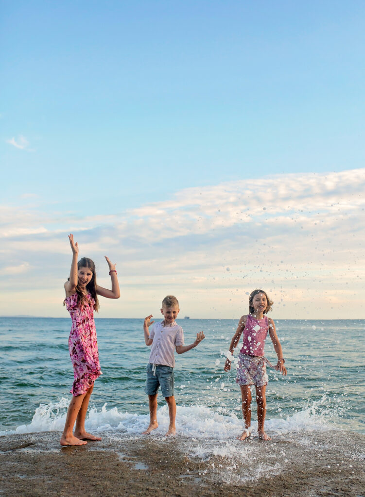 3 siblings getting splashed by the waves standing on a rock
