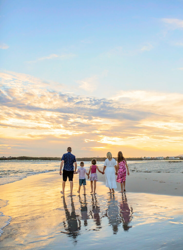 a family of 5 walk along the beach at sunset
