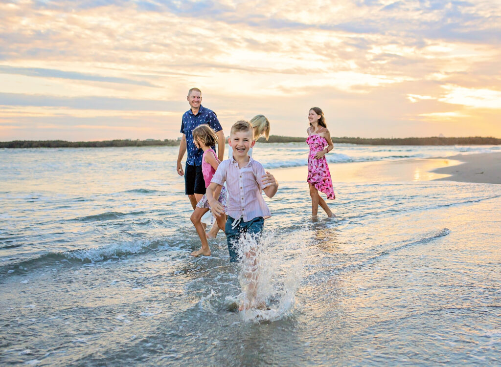 a family of 5 in the shallow water on the beach. the young boy is splashing and smiling