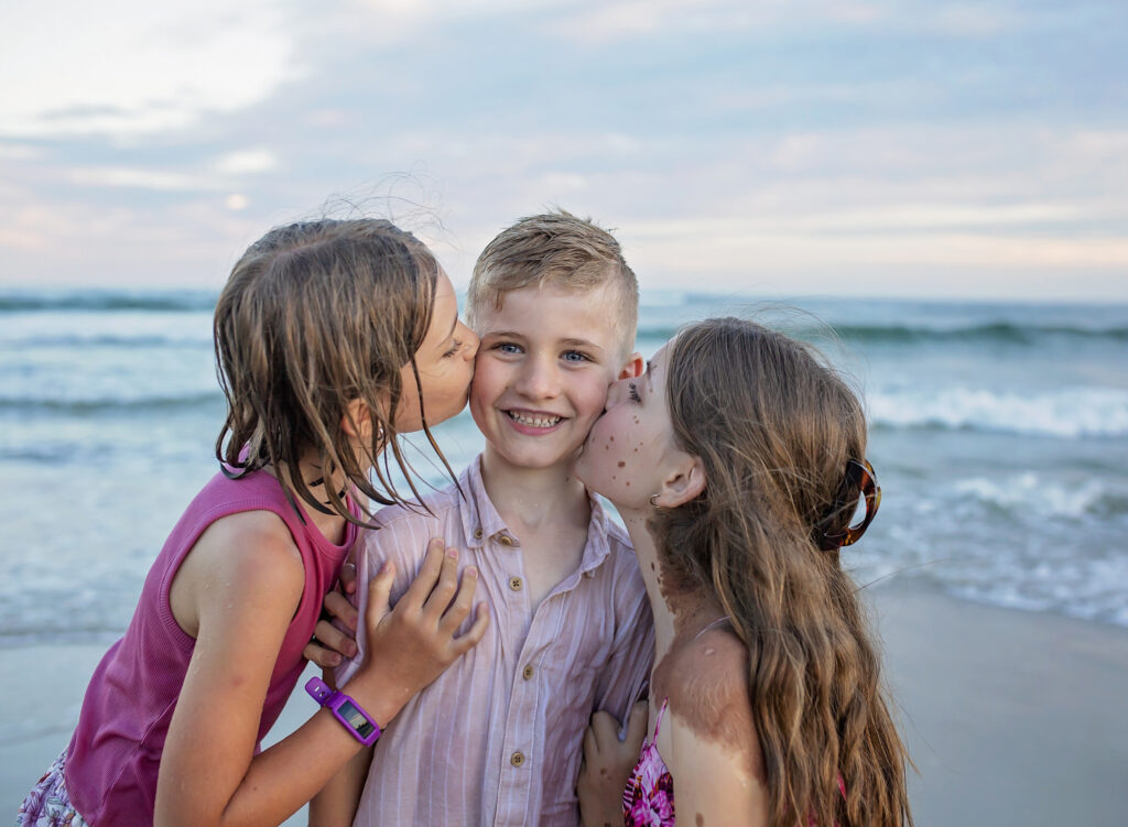 two sisters kissing their brother on his cheeks on the beach